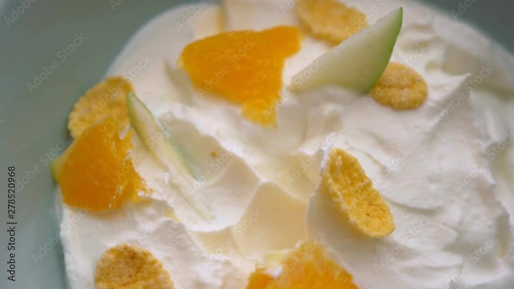 Closeup macro shoot of hand dipping a spoon in sweet yogurt breakfast bowl with fruits and cornflakes Closeup macro shoot of hand dipping a spoon in sweet yogurt breakfast bowl with fruits and cornflakes