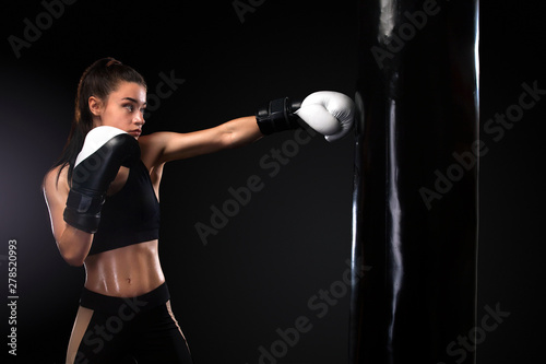 Woman boxer fighting in gloves with boxing punching bag on black background. Boxing and fitness concept. © Mike Orlov