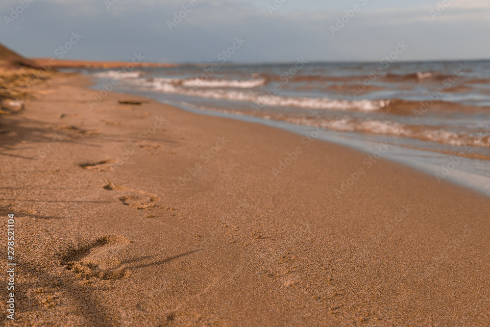 Footprints leaving the distance on the sand with waves washing the beach at sunset Footprints leaving the distance on the sand with waves washing the beach at sunset