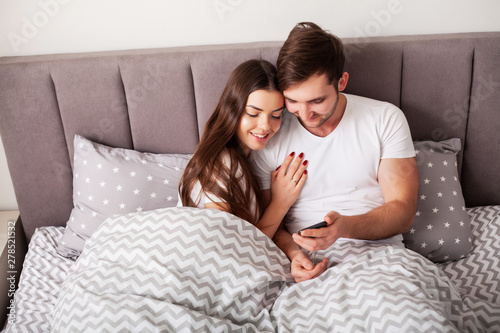 Smiling young couple taking selfie together in bedroom