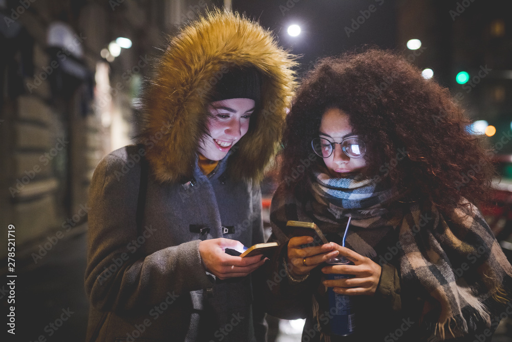 two young women standing in the street and interacting with smartphone