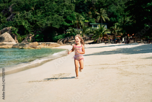 Pretty little girl running on ocean beach in tropical island