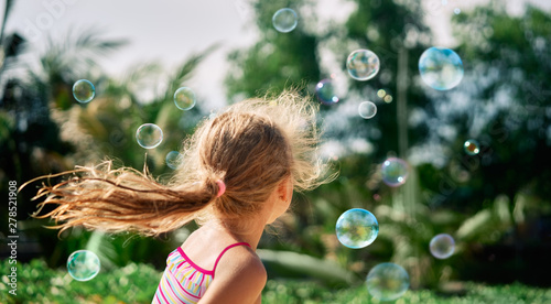 Back view of happy little girl playing soap bubbles on the nature