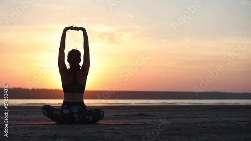 woman silhouette practicing yoga asana and improving physical and mental health sitting by sea at sunset backside view