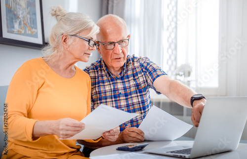 Worried senior couple checking bills using laptop at home