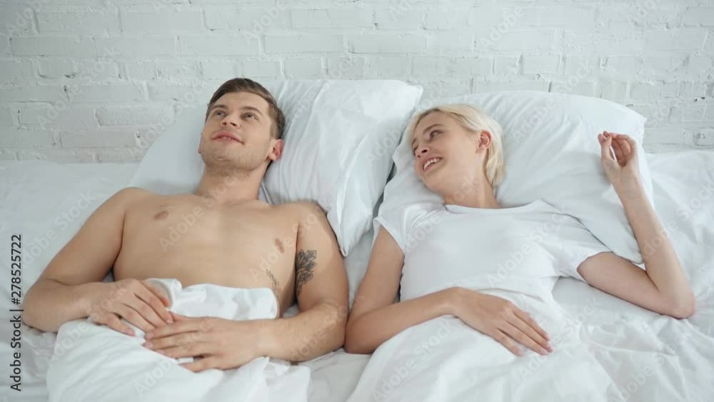 handsome man talking and kissing beautiful smiling woman in bed