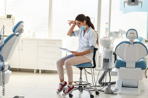 Female dentist in dental office .She tired after hard work, sitting on chair and planing list of exams for next working day.