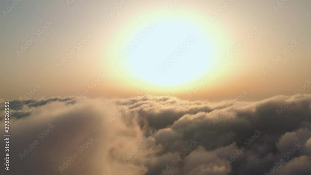 Scenic aerial view of moving white clouds. The drone flies high back in the blue sky through the fluffy clouds in the evening at the bright sun. The sun is hidden behind the clouds at sunset Scenic aerial view of moving white clouds. The drone flies high back in the blue sky through the fluffy clouds in the evening at the bright sun. The sun is hidden behind the clouds at sunset