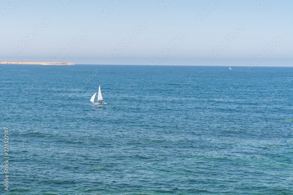 A lonely sailboat sailing on a blue calm sea on a sunny summer day A lonely sailboat sailing on a blue calm sea on a sunny summer day