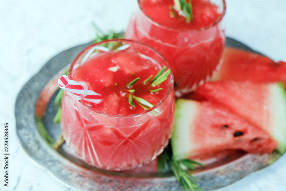 Two glasses of refreshing beverage and watermelon slices. Summer cocktail with watermelon juice and rosemary.