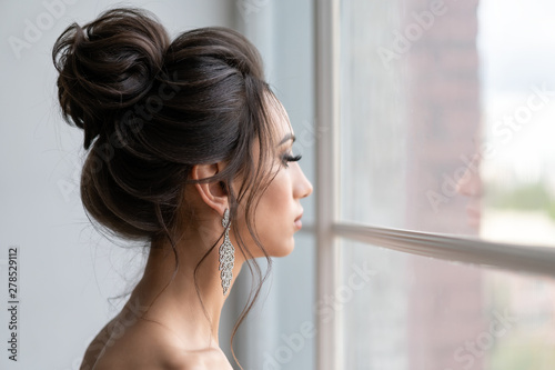 beautiful girl with hairstyle high beam looks out window. Evening image girl.