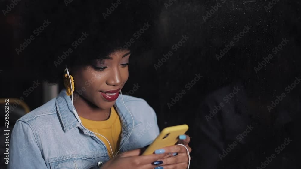 Attractive young african american woman using smartphone riding at public transport. Night time. City lights background. Attractive young african american woman using smartphone riding at public transport. Night time. City lights background.