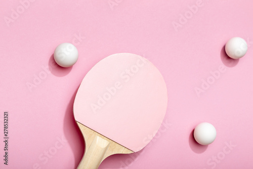 top view of white table tennis balls scattered near pink racket on pink background