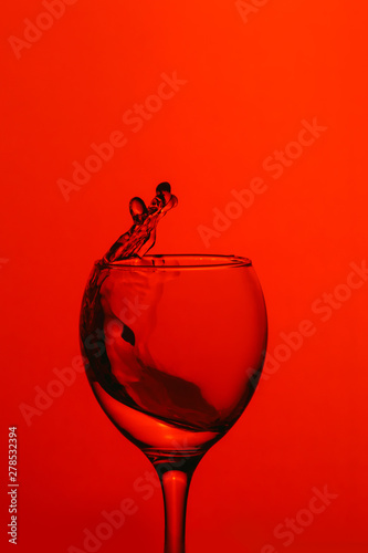 splash of water in wineglass isolated on red background.