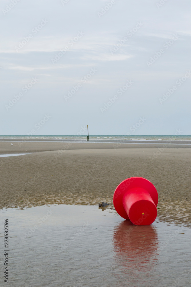 Bouée rouge posée sur le sable à marée basse sous un ciel gris. Côte belge Bouée rouge posée sur le sable à marée basse sous un ciel gris. Côte belge