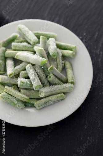 frozen green beans on white plate on ceramic background