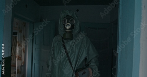 Man in Vintage WWII Hazmat suit and gas mask standing in the doorway of a house. The dosimeter in the Chernobyl zone checks the state of the buildings and the level of radiation pollution.