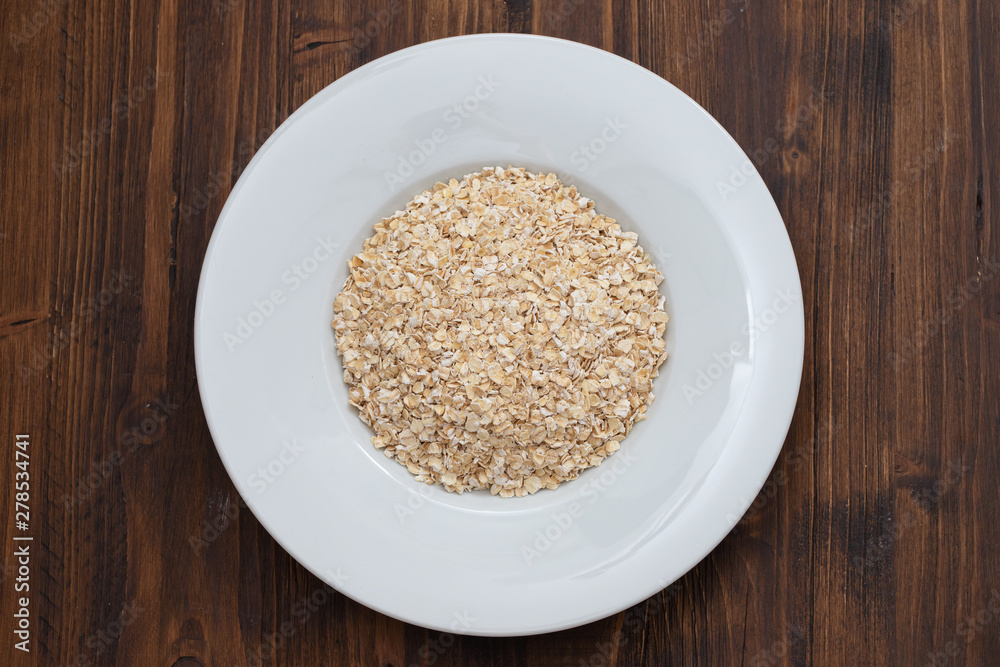 uncooked oats in white plate on wooden background uncooked oats in white plate on wooden background