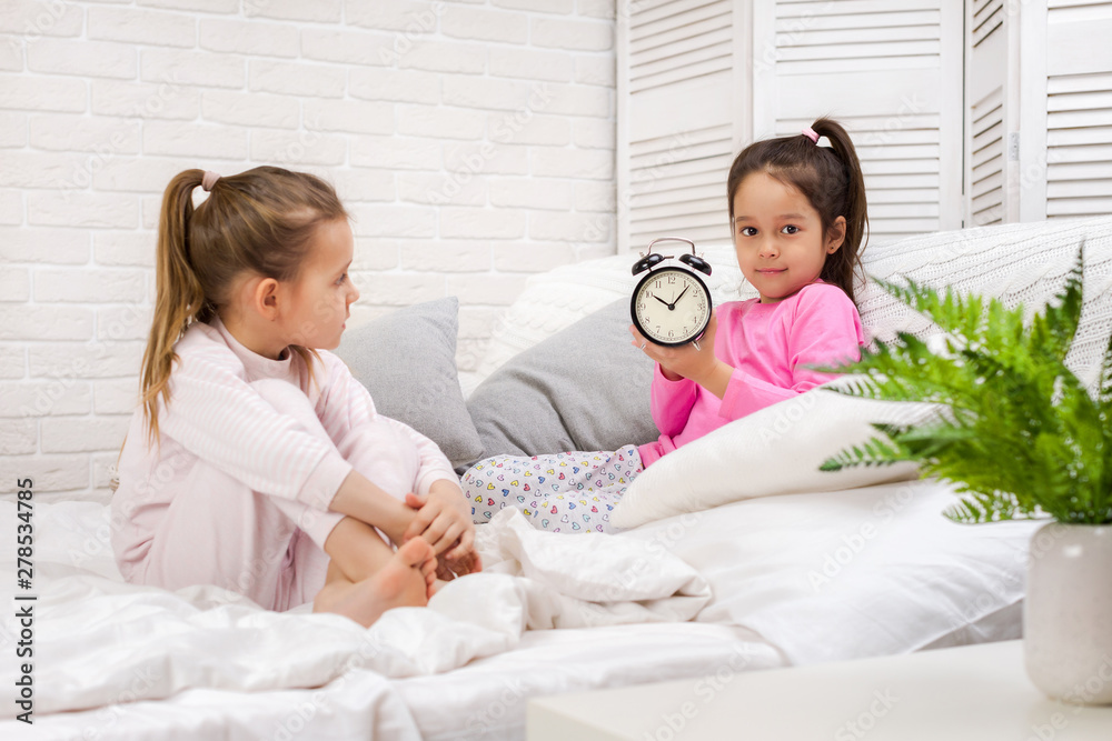 two cute children girls with clock in bed in the morning two cute children girls with clock in bed in the morning