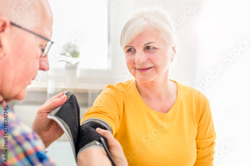 Senior husband doing blood pressure measurement to his wife at home