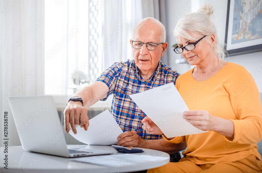 Senior couple checking bills using laptop at home Senior couple checking bills using laptop at home
