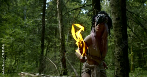 wild female hunter with torch in hand is moving in forest warily in daytime