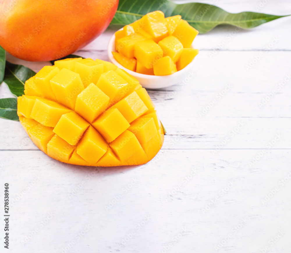 Beautiful chopped mango chunks with green leaves on bright white color timber background. Copy space, close up, macro. Tropical fruit concept. Beautiful chopped mango chunks with green leaves on bright white color timber background. Copy space, close up, macro. Tropical fruit concept.