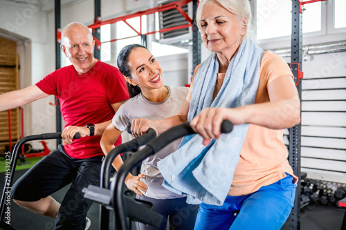 Senior couple biking at the gym with personal trainer