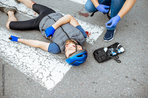 Road accident with injured cyclist on the pedestrian crossing with passerby pedestrian providing first aid