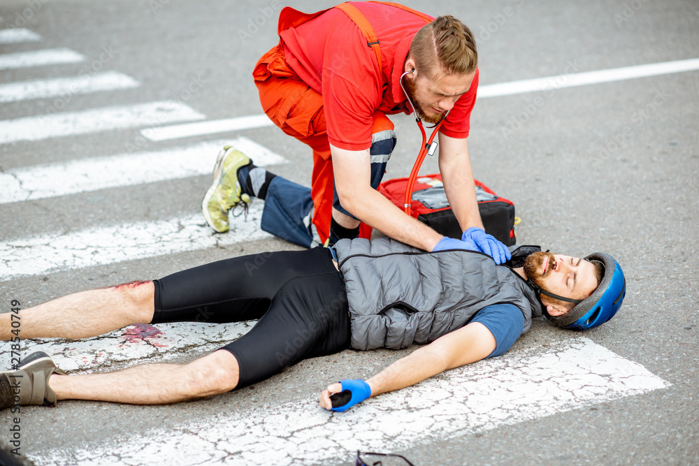 Medic applying first aid to the injured cyclist lying on the pedestrian crossing after the road accident