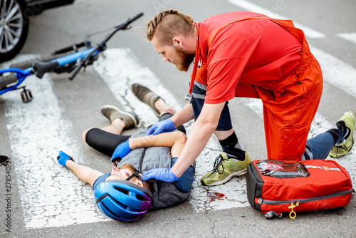 Medic applying first aid to the injured cyclist lying on the pedestrian crossing after the road accident