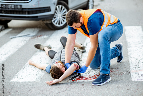 Man applying first aid to the injured bleeding person, wearing tourniquet on the arm after the road accident on the pedestrian crossing