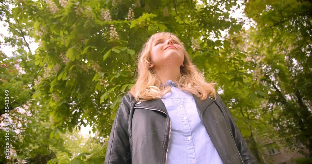 Down top shot of pretty caucasian blonde student standing in the green park observing the beauty of nature. Down top shot of pretty caucasian blonde student standing in the green park observing the beauty of nature.