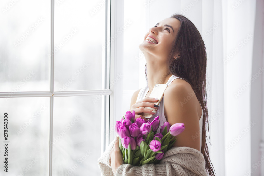Attractive young woman with flowers indoors in the bedroom. Portrait of beautiful lady at home. Close up shot of female with tulips. Attractive young woman with flowers indoors in the bedroom. Portrait of beautiful lady at home. Close up shot of female with tulips.