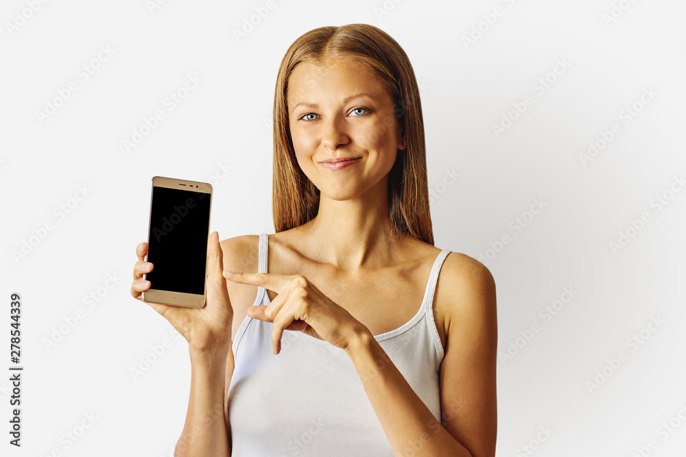 Happy smiling woman points at smartphone, isolated over light grey background