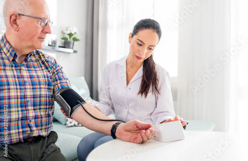 Nurse visiting senior male at home doing blood pressure measurement