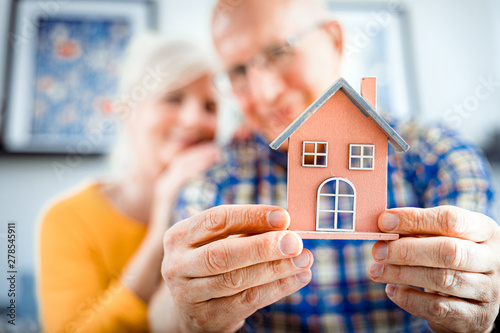 Canvas Print New house concept, happy senior couple holding small home model