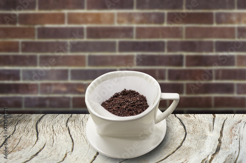 cup of drip coffee with paper filter tool on wood table and brick wall