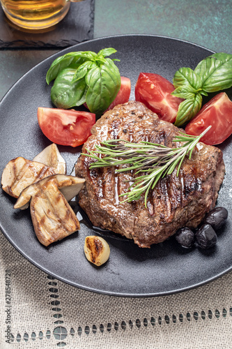 Grilled beef steak with mushrooms and vegetables on black plate, cliseup photo