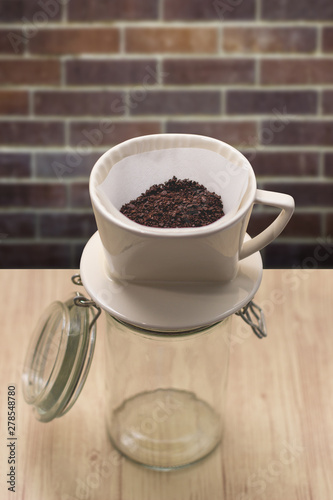 cup of drip coffee with paper filter tool on wood table and brick wall