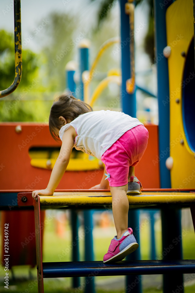 Fototapeta premium Adorable little 1-2 year old Asian toddler girl having fun on playground. View from behind toddler trying to climb the stairs.