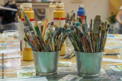 Set of paintbrushes multi-colored on the cup. Paint brushes and paints for drawing. Interior of the art school for drawing children. Creativity and people concept.