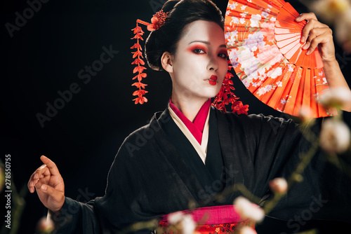 Foto selective focus of geisha in black kimono with red flowers in hair holding hand