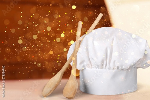 White cooks cap and wooden spoons on wooden table