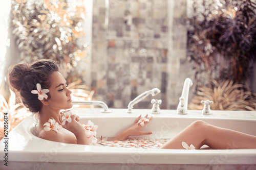 Fotografia Pretty girl enjoying bath with plumeria tropical flowers