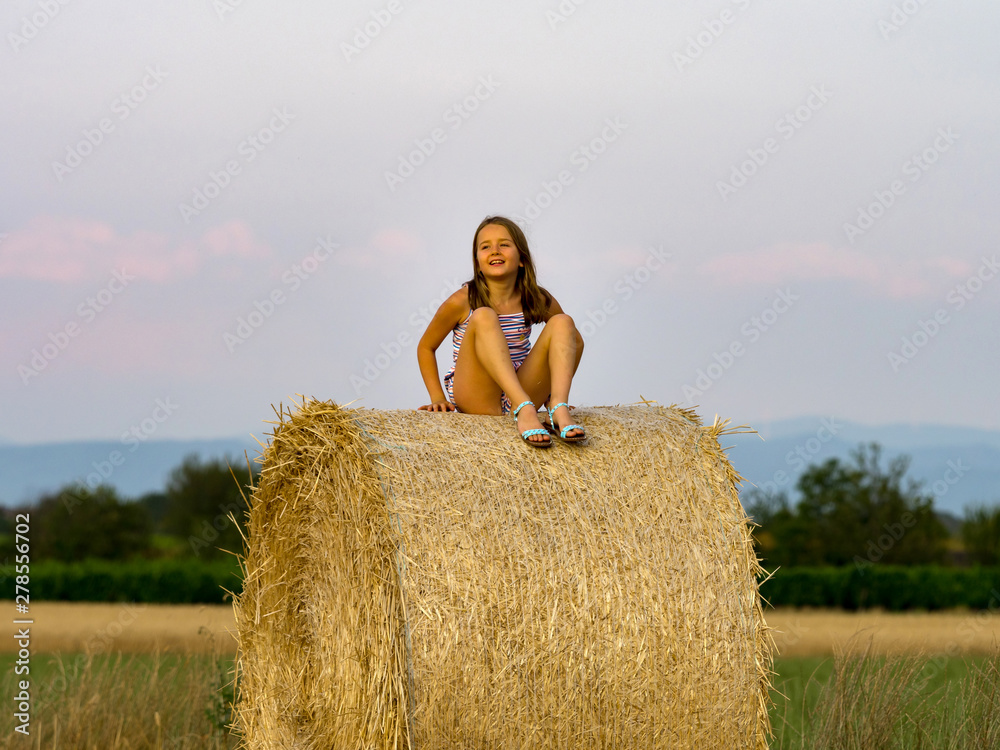 The little girl sits on a haystack in the twilight of day The little girl sits on a haystack in the twilight of day
