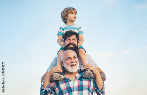 Men generation: grandfather father and grandson are hugging looking at camera and smiling. Fathers day concept. Generation concept. Weekend family play. Men in different ages. photo