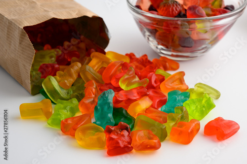 Glass bowls and paper bag of colorful gummy candies on white background