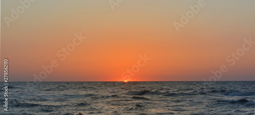 The sun sets in the sea on a clear evening