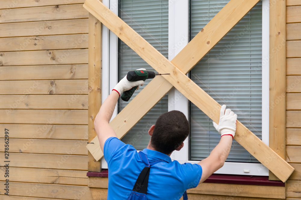 worker blocks the windows with boards to protect them from natural disasters worker blocks the windows with boards to protect them from natural disasters
